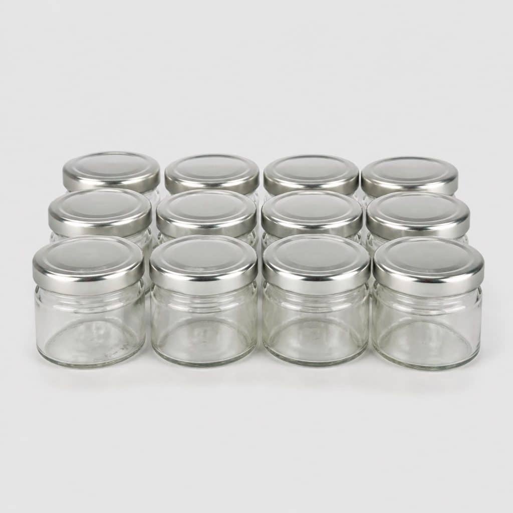 Douze petits pots en verre avec couvercle alignés sur fond clair
